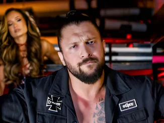 Karrion Kross blickt streng in die Kamera, während sich Scarlett im Hintergrund befindet