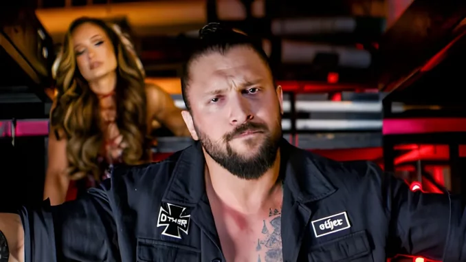 Karrion Kross blickt streng in die Kamera, während sich Scarlett im Hintergrund befindet