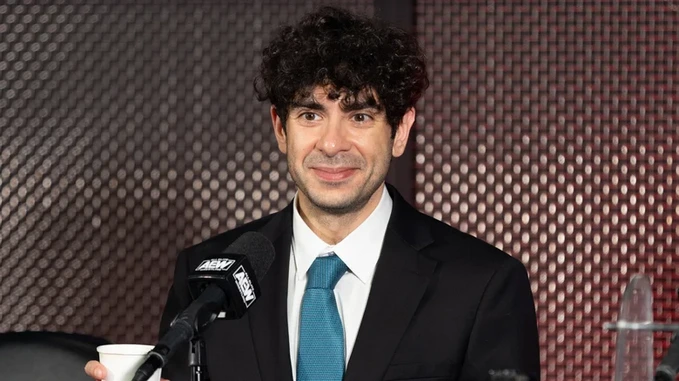 Tony-Khan-steht-Rede-und-Antowrt-und-beantwortet-Fragen Tony Khan vor einem Standmikrofon