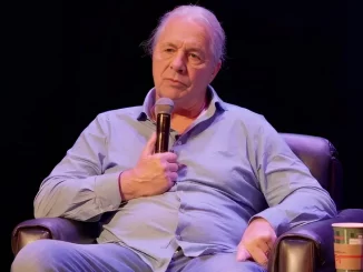 Bret Hart sitzt in einem Sessel und hält ein Mikrofon in der Hand