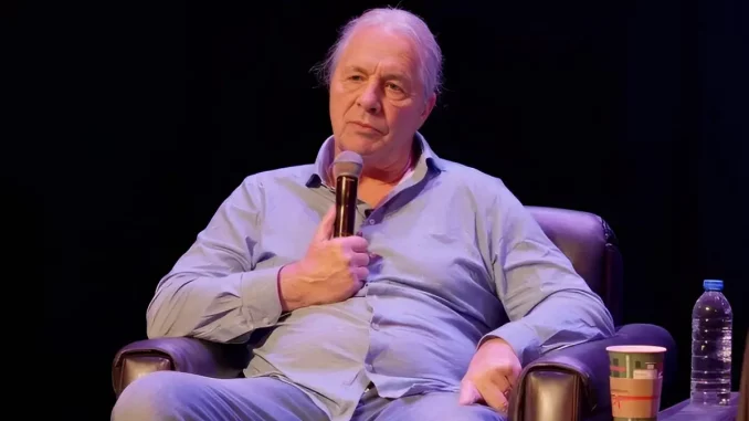 Bret Hart sitzt in einem Sessel und hält ein Mikrofon in der Hand