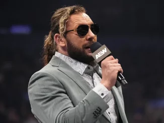 Kenny Omega steht im Ring und hält ein AEW Mikrofon in der rechten Hand