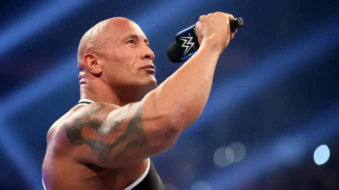The Rock steht für seine Promo im WWE-Ring und hält ein Mikrofon in der rechten Hand