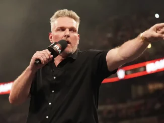 Pat McAfee steht in einer Arena mit Mikrofon in der Hand und zeigt energisch mit ausgestrecktem Arm ins Publikum