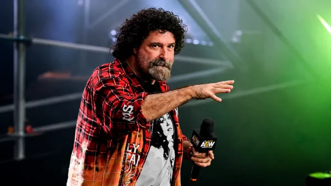 Mick Foley hält ein Mikrofon und erhebt seine Hand