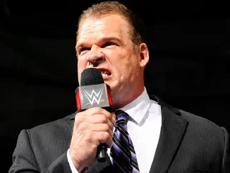 Kane steht im Anzug im Ring und hält während einer intensiven Promo ein WWE-Mikrofon in der Hand und blickt mit wütendem Gesichtsausdruck in die Menge