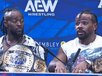 Kofi und Austin Creed sitzen bei einer Pressekonferenz vor einer blauen AEW Wrestling-Kulisse, während vor ihnen ihre goldenen AEW Tag Team Trios Champion-Titel auf dem Tisch liegen