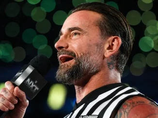 CM Punk spricht mit einem NXT-Mikrofon in der Hand vor einem unscharfen, von grünen Arena-Lichtern geprägten Hintergrund
