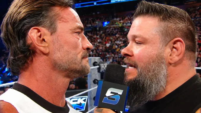 CM Punk steht im Ring und starrt Kevin Owens direkt an, der ein Mikrofon in der Hand hält und spricht