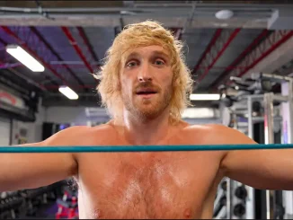 Logan Paul steht mit ausgestreckten Armen in einem Trainingsring hinter einem türkisfarbenen Seil und blickt direkt in die Kamera