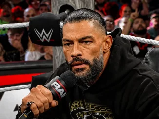 Roman Reigns sitzt mit ernstem Blick im Ring und spricht in ein RAW-Mikrofon, während im Hintergrund zahlreiche Zuschauer zu sehen sind