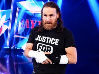 Sami Zayn steht auf der Bühne und hält seine Armschiene fest