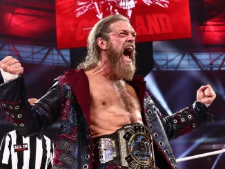 Adam Copeland steht mit der AEW Tag Team Championship um die Hüfte im Ring und jubelt mit erhobenen Fäusten vor der rot beleuchteten Arena-Kulisse