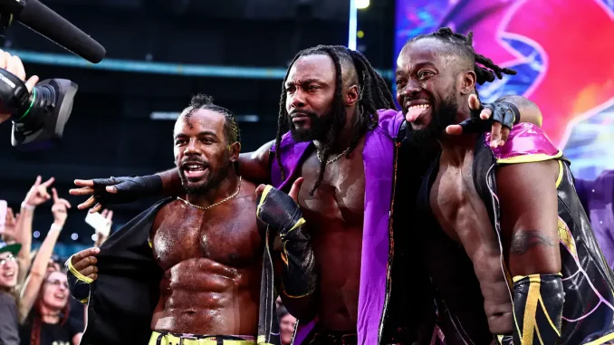 Austin Creed, Kofi und Swerve Strickland stehen nach einem Match eng beieinander, während sie vor jubelnden Fans und laufenden Kameras gemeinsam für einen ausgelassenen Moment posieren