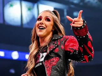 Britt Baker in einer schwarz-roten, glitzernden Jacke zeigt während ihres Auftritts in einer beleuchteten Arena mit der Hand ins Publikum