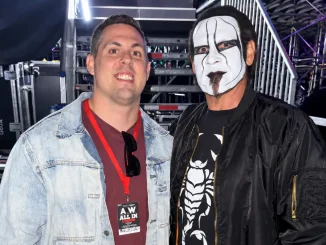 Das Bild zeigt Garrett Borden und Sting backstage bei einer AEW-Veranstaltung, wobei beide nebeneinander vor Produktions- und Bühnentechnik für die Kamera posieren