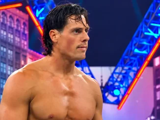 Steven Borden steht oberkörperfrei mit konzentriertem Blick vor einer farbenfrohen Wrestling-Kulisse mit blauen und roten Lichtelementen