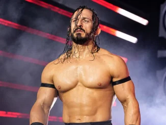 PAC steht mit nassen Haaren und ernstem Blick vor der rot beleuchteten, nebelverhangenen Kulisse einer Wrestling-Arena