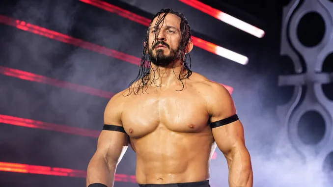 PAC steht mit nassen Haaren und ernstem Blick vor der rot beleuchteten, nebelverhangenen Kulisse einer Wrestling-Arena