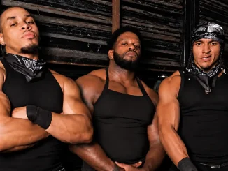 Das neue WWE-Stable 946 posiert vor einer dunklen Industriewand, mit Royce Keys in der Mitte und den beiden OTM-Mitgliedern an seiner Seite