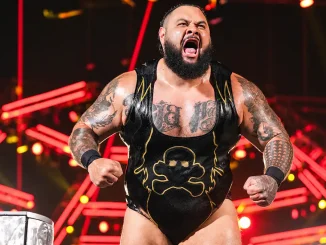 Bronson Reed ist mit geballten Fäusten und lautem Schrei in seiner schwarzen Wrestling-Kleidung vor einer auffällig rot beleuchteten Arena-Kulisse zu sehen