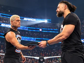 Cody Rhodes und Roman Reigns stehen sich im WWE-Ring gegenüber und halten gemeinsam eine schwarze Mappe zwischen sich, während sie sich ernst ansehen