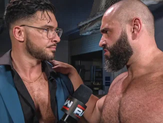 Ethan Page steht in einem Backstage-Bereich mit einem WWE-Mikrofon neben Rusev, der ihm die Hand auf die Schulter legt, während sich beide mit ernster Miene direkt ansehen