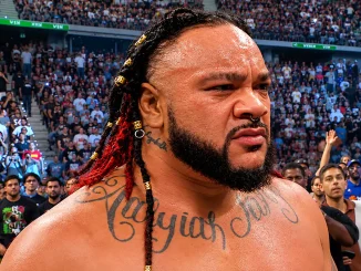 Jacob Fatu steht mit ernstem, konzentriertem Blick inmitten einer voll besetzten Arena, während die Zuschauer dicht hinter ihm für eine intensive Wrestling-Atmosphäre sorgen