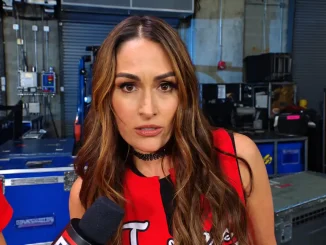 Nikki Bella ist bei einem Backstage-Interview zu sehen, während sie in einem rot-schwarzen Outfit direkt in die Kamera blickt und vor ihr ein Mikrofon gehalten wird
