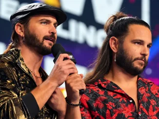 The Young Bucks, Matt und Nick Jackson, stehen gemeinsam in der Arena, während einer von beiden mit einem Mikrofon spricht und der andere ernst danebensteht.