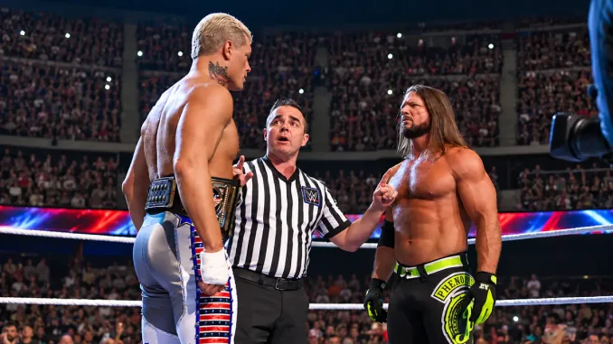 Cody Rhodes und AJ Styles stehen sich im Wrestlingring angespannt gegenüber, während der Ringrichter zwischen beiden vermittelt und die voll besetzte Arena im Hintergrund zu sehen ist.