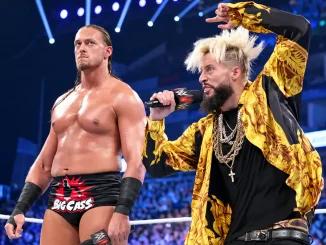 Big Cass steht mit ernstem Blick im WWE-Ring, während Enzo Amore neben ihm mit einem Mikrofon spricht und dabei gestikuliert.