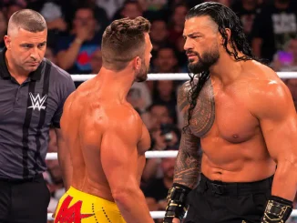 Roman Reigns und LA Knight stehen sich im WWE-Ring angespannt gegenüber, während ein Ringrichter das Geschehen aufmerksam beobachtet.
