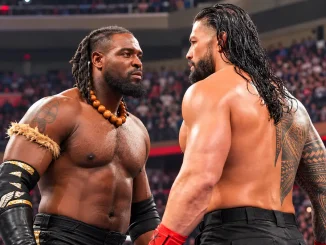 Oba Femi und Roman Reigns stehen sich in einer WWE-Arena angespannt gegenüber. Beide Wrestler blicken sich ernst in die Augen, während im Hintergrund zahlreiche Zuschauer zu sehen sind.