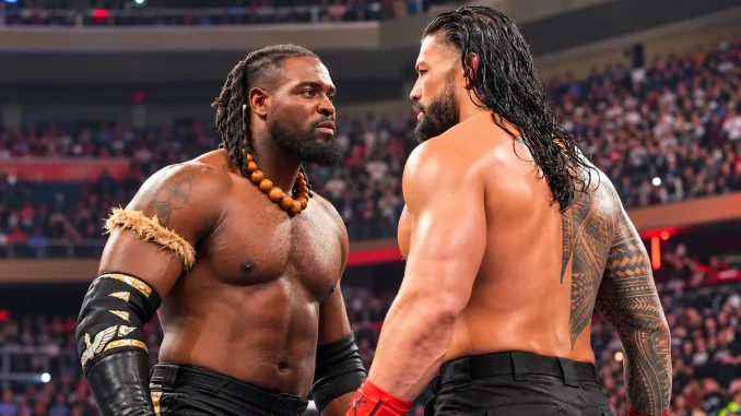 Oba Femi und Roman Reigns stehen sich in einer WWE-Arena angespannt gegenüber. Beide Wrestler blicken sich ernst in die Augen, während im Hintergrund zahlreiche Zuschauer zu sehen sind.
